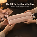Hands passing a blush pink velvet mahjong rack bag across a table, with pink tissue paper and ribbon