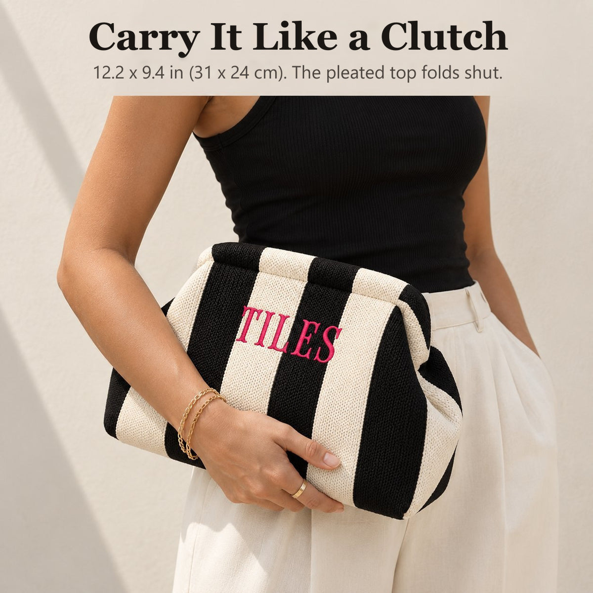 Woman carrying a black and ivory striped mahjong tile bag as a clutch, embroidered "Tiles" in hot pink
