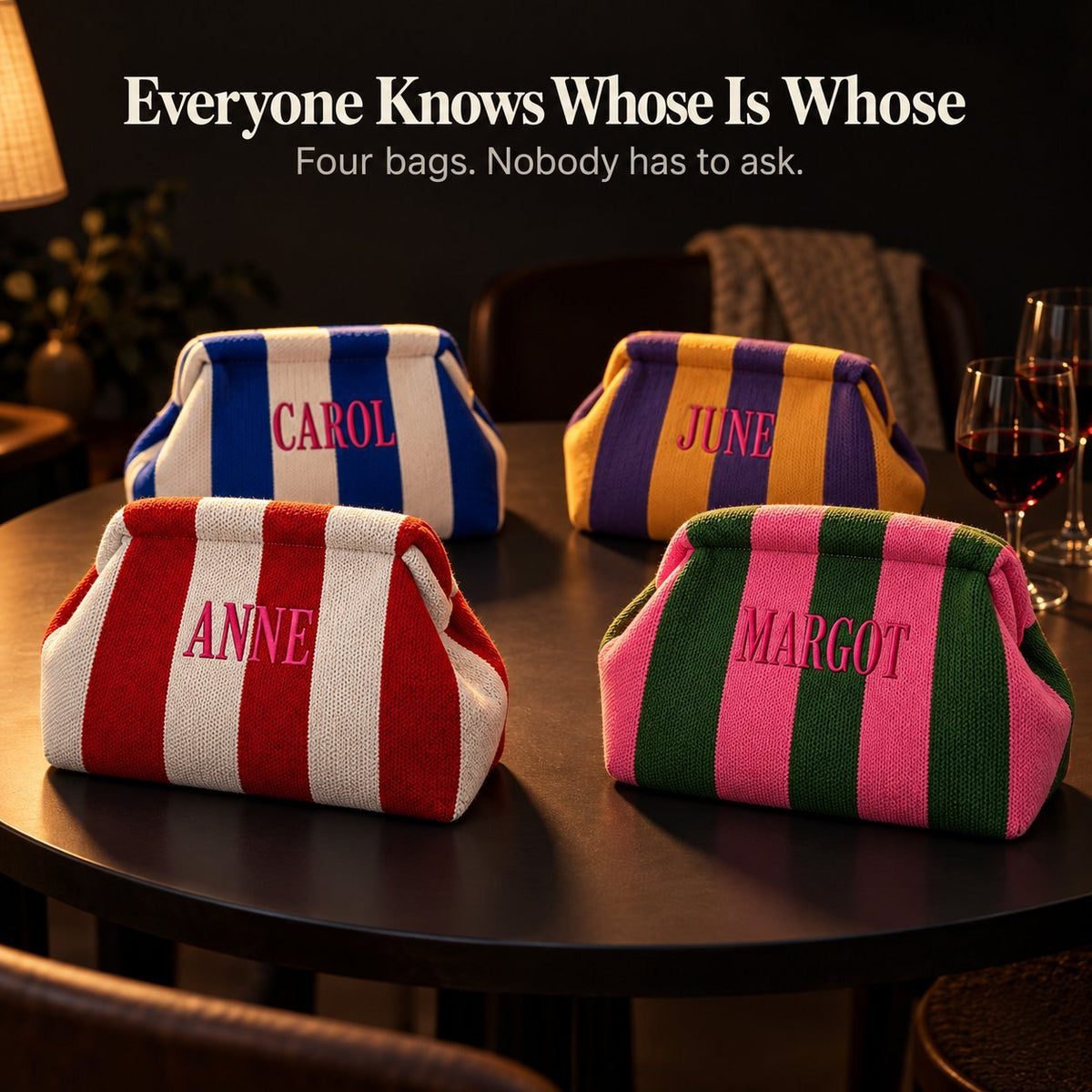 Four striped mahjong tile bags embroidered "Carol", "June", "Anne" and "Margot" on a dark table beside wine glasses