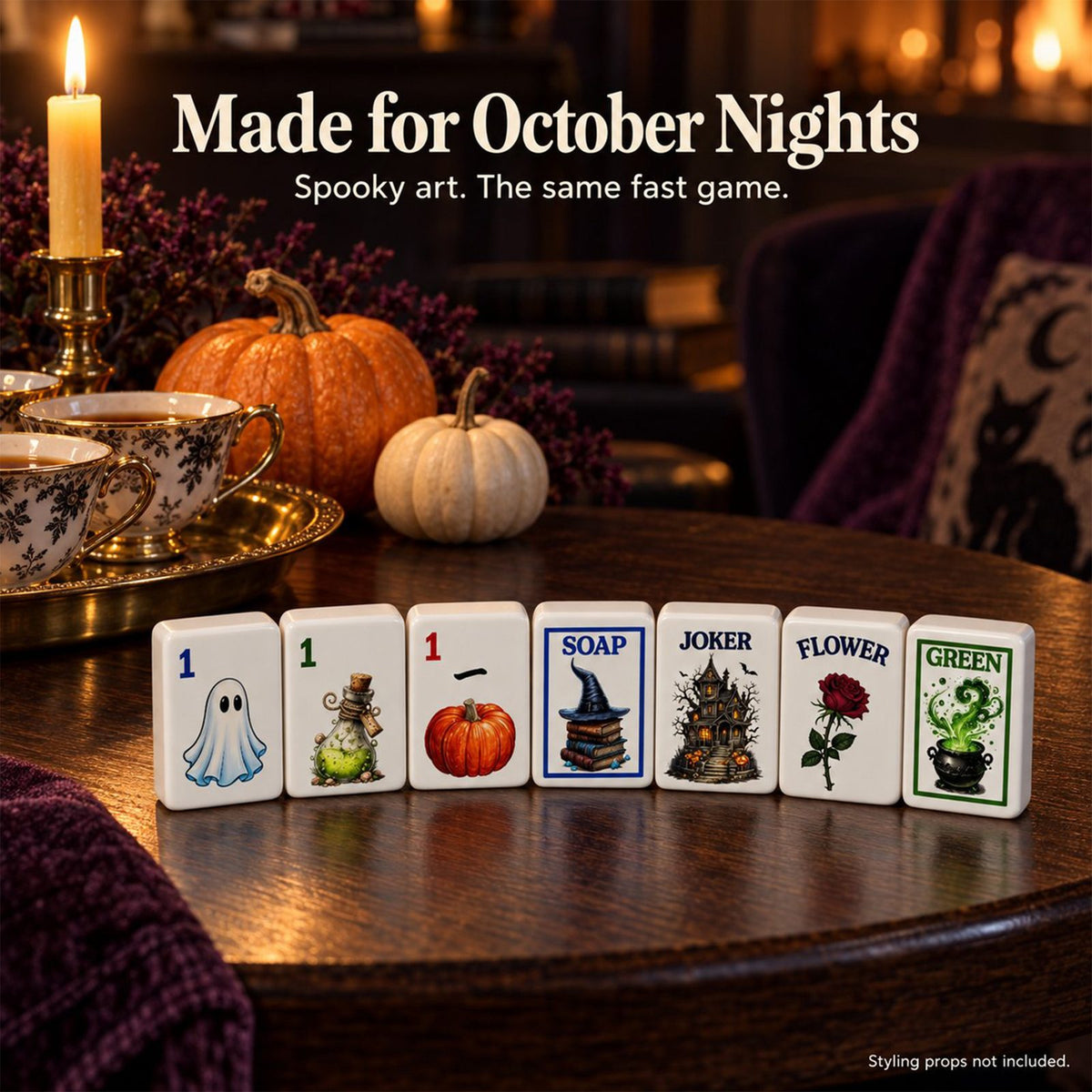 Row of Halloween mahjong tiles on a round wooden table with candles, teacups and pumpkins