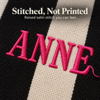 Close-up of hot pink raised embroidery spelling "Anne" across black and cream stripes of a mahjong tile bag